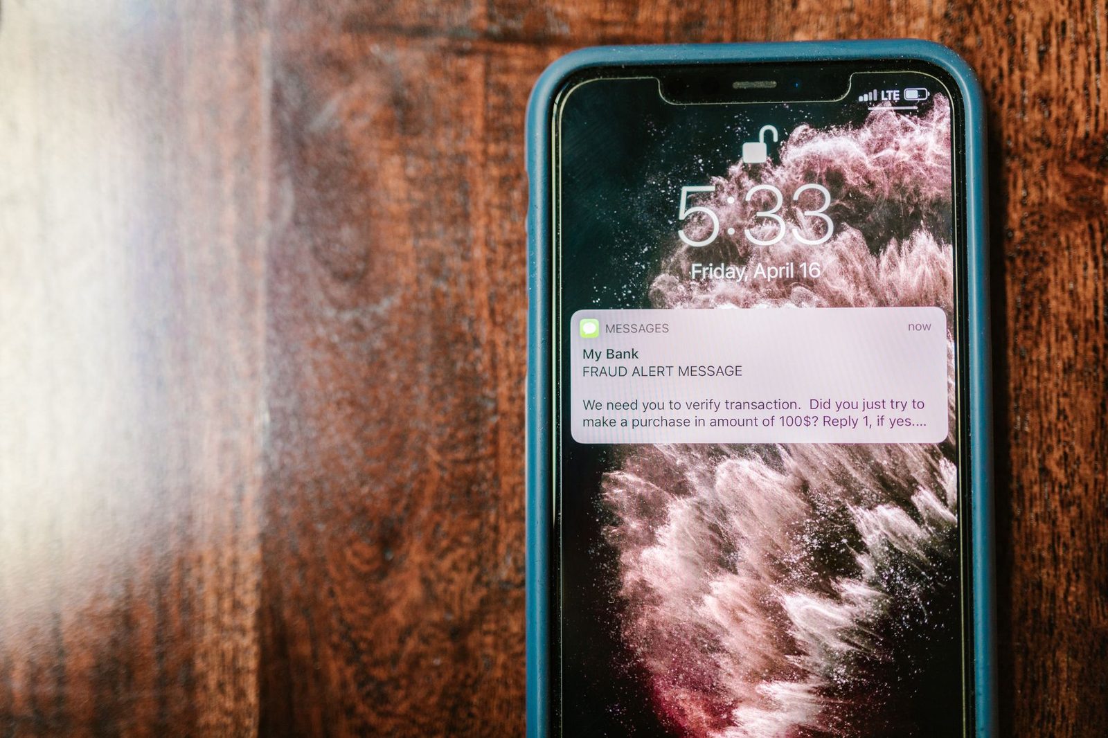 Smartphone posé sur une table en bois affichant une notification SMS d'alerte de fraude bancaire