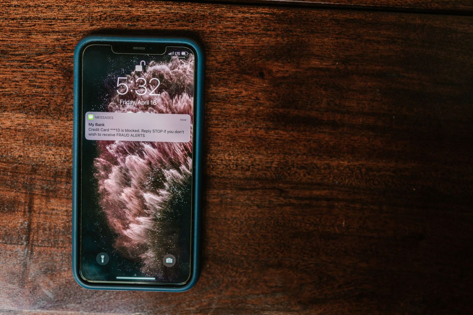 Smartphone op een houten tafel met een sms-melding van een bankwaarschuwing op het vergrendelscherm