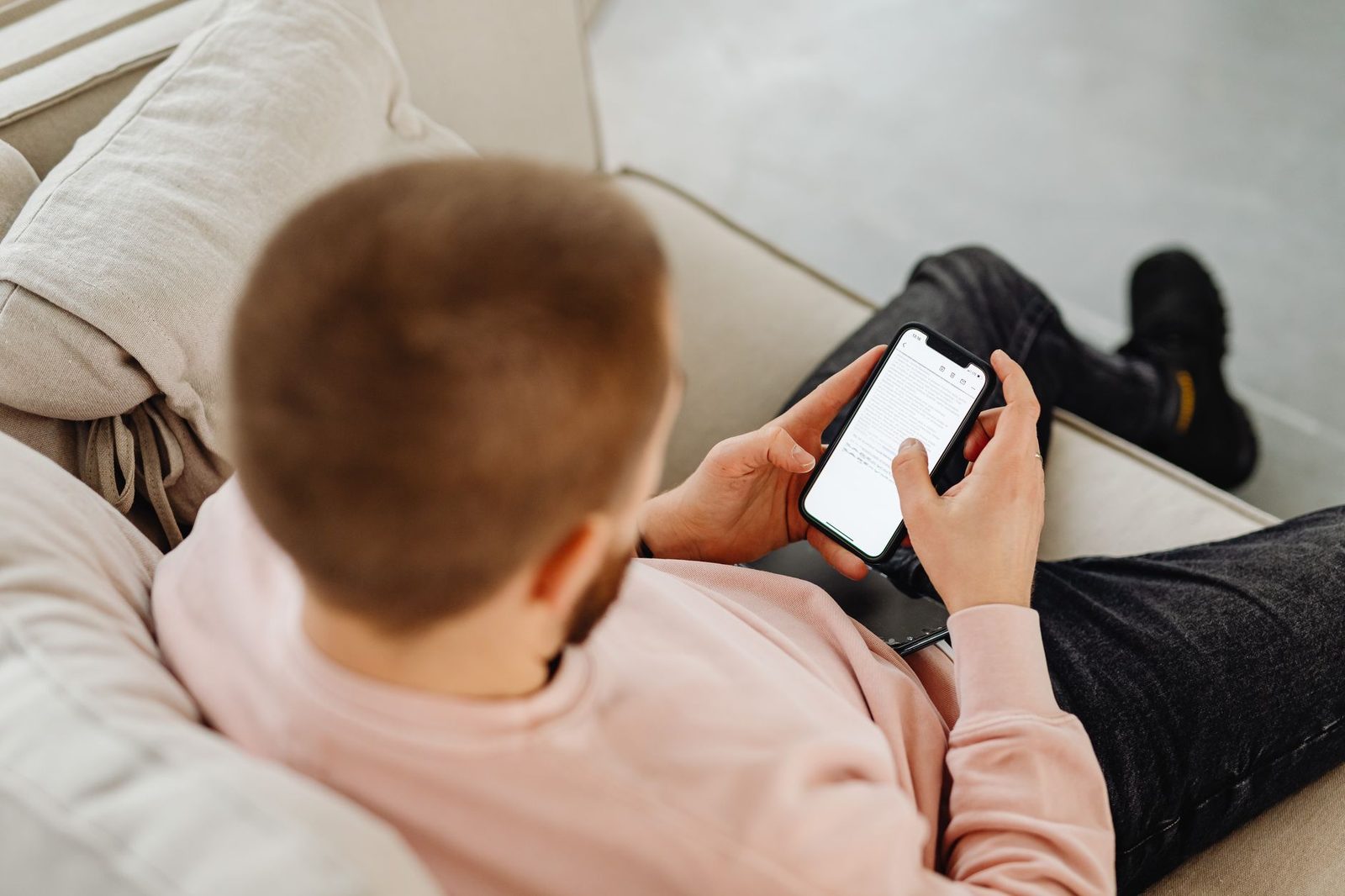 Man op een bank die een bericht op het scherm van zijn mobiele telefoon leest, van achteren gezien