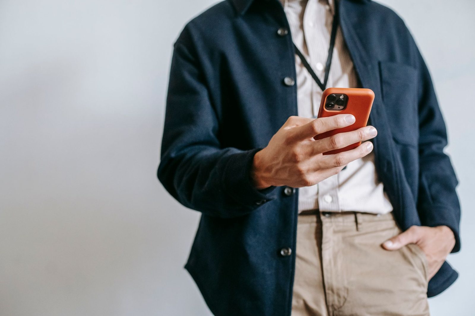 Man in a blue jacket holding a smartphone in an orange case, against a light background