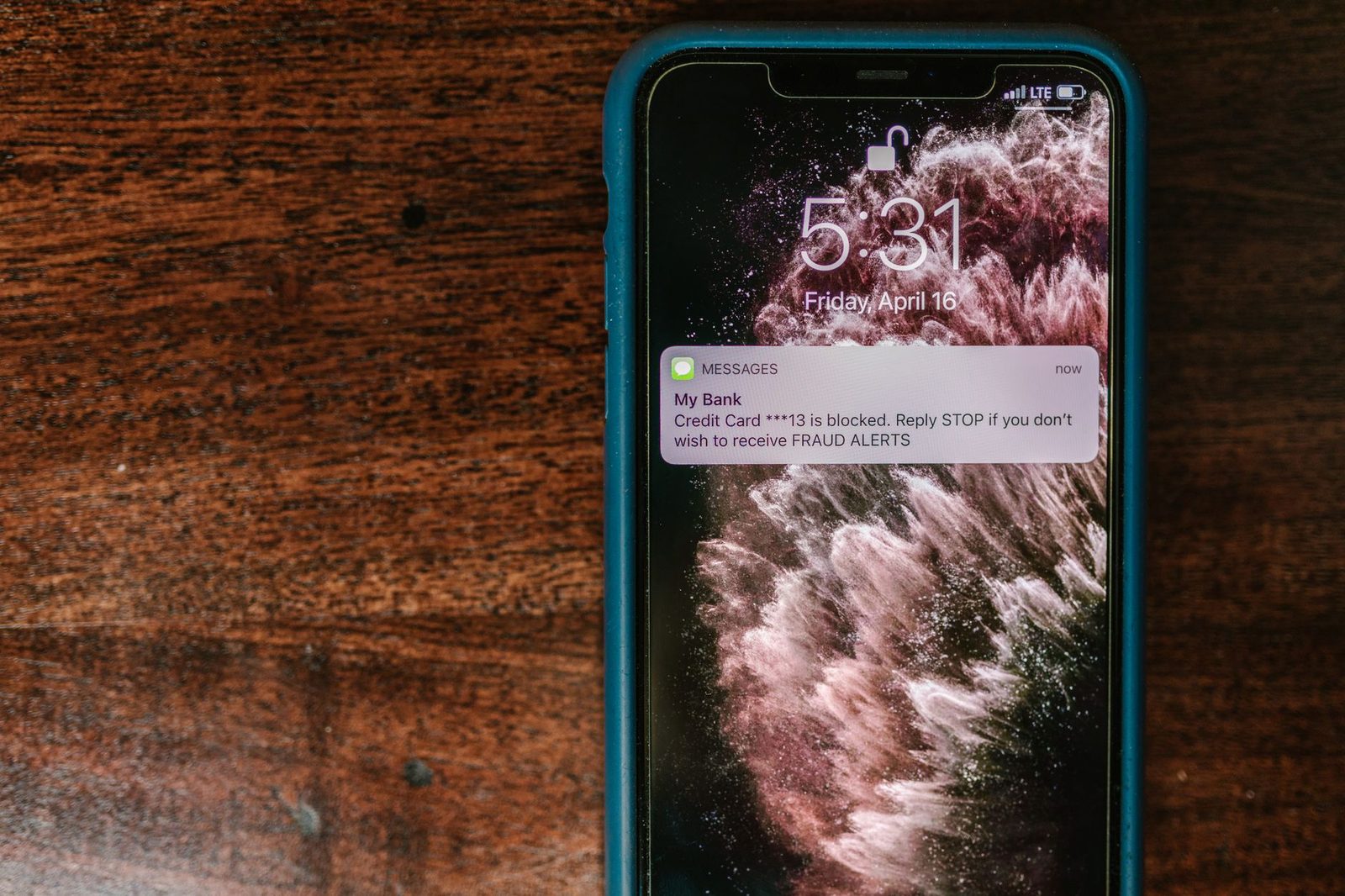 Smartphone lying on a wooden table displaying a fraudulent text message notification claiming to come from a bank