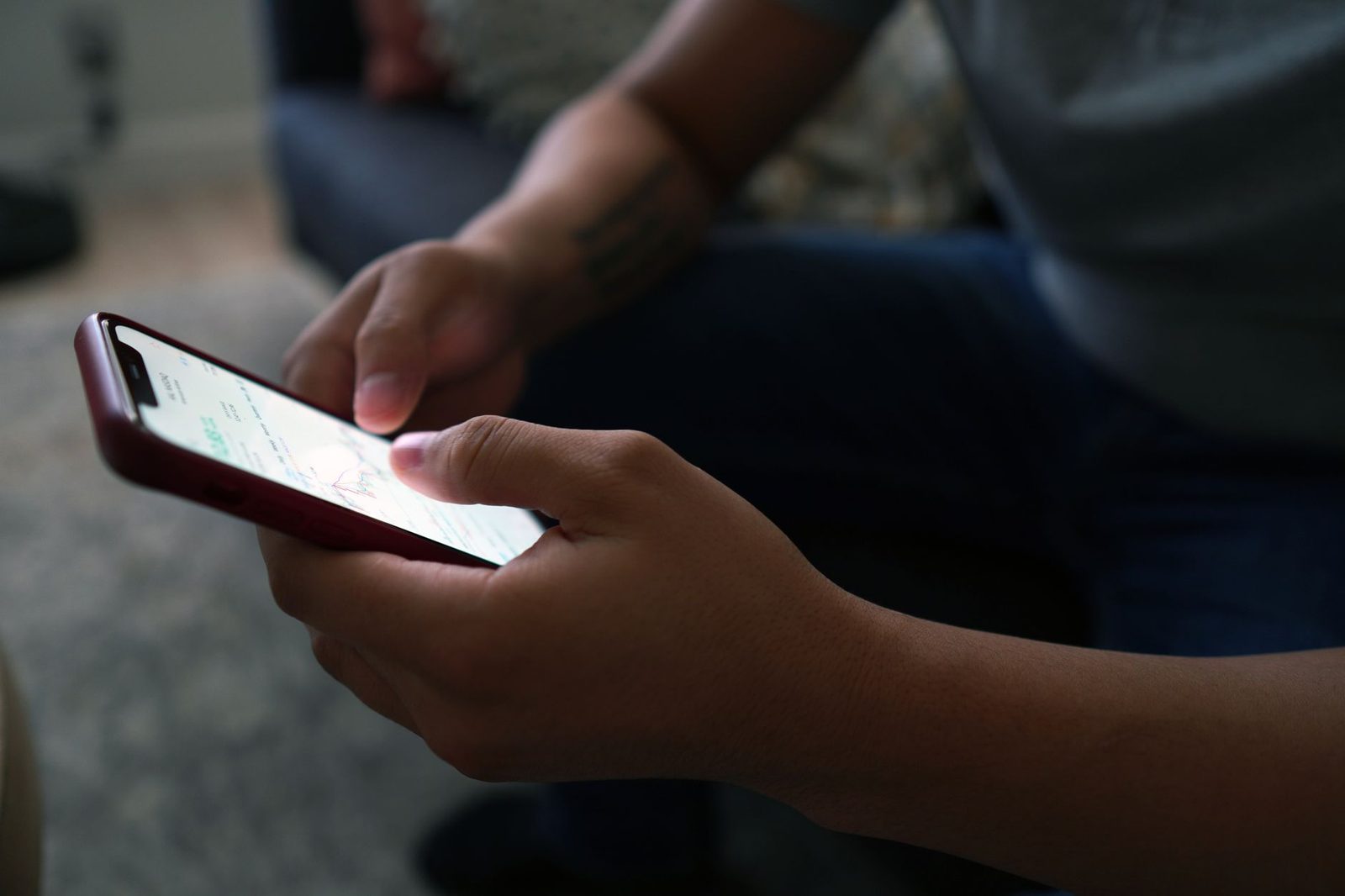 Personne assise tenant un smartphone à coque rouge dans ses deux mains et consultant l'écran allumé