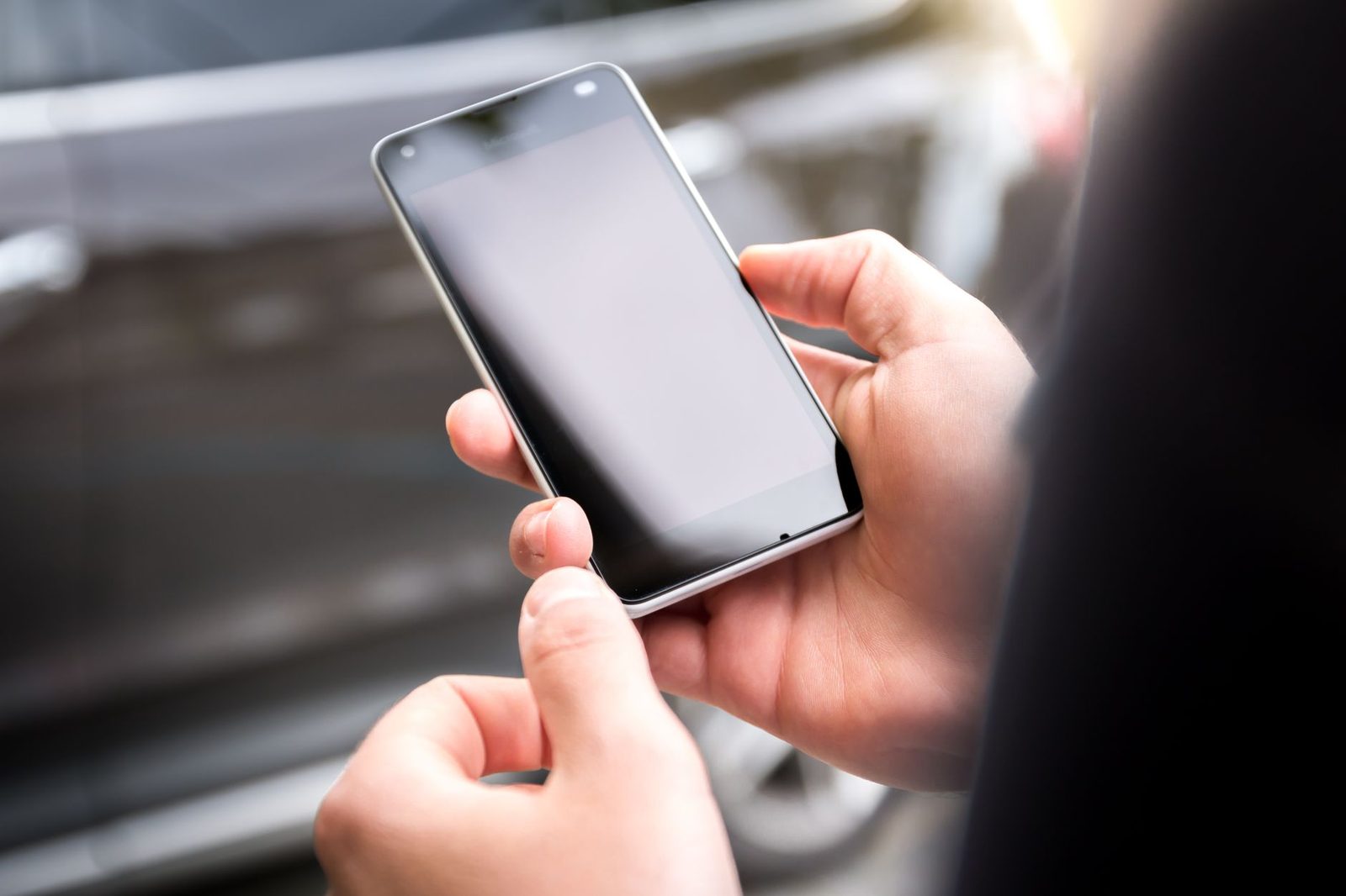 Gros plan sur les mains d'une personne tenant un smartphone à l'écran noir en extérieur
