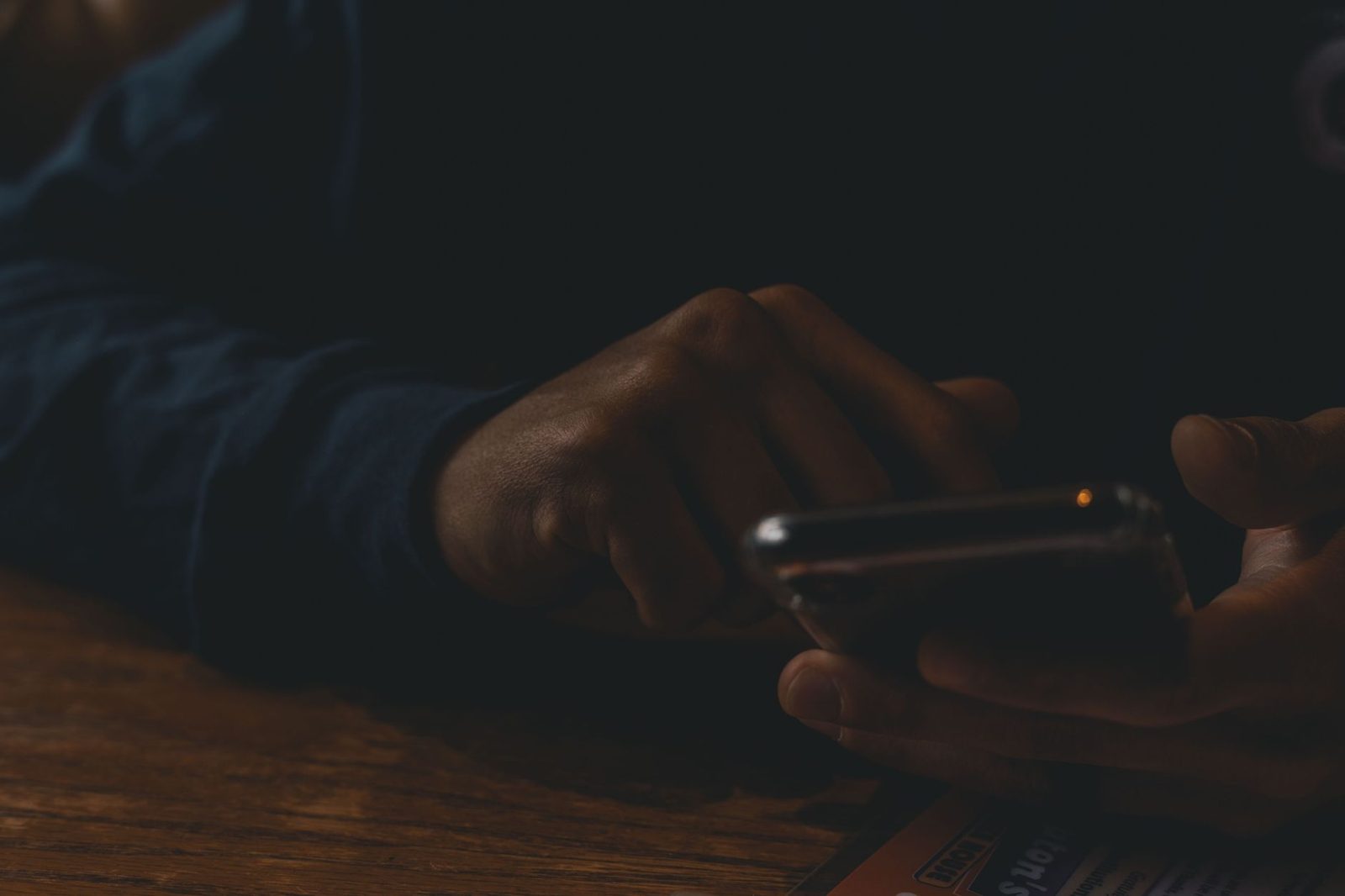 Gros plan sur les mains d'une personne utilisant un smartphone dans la pénombre, posée sur une table en bois