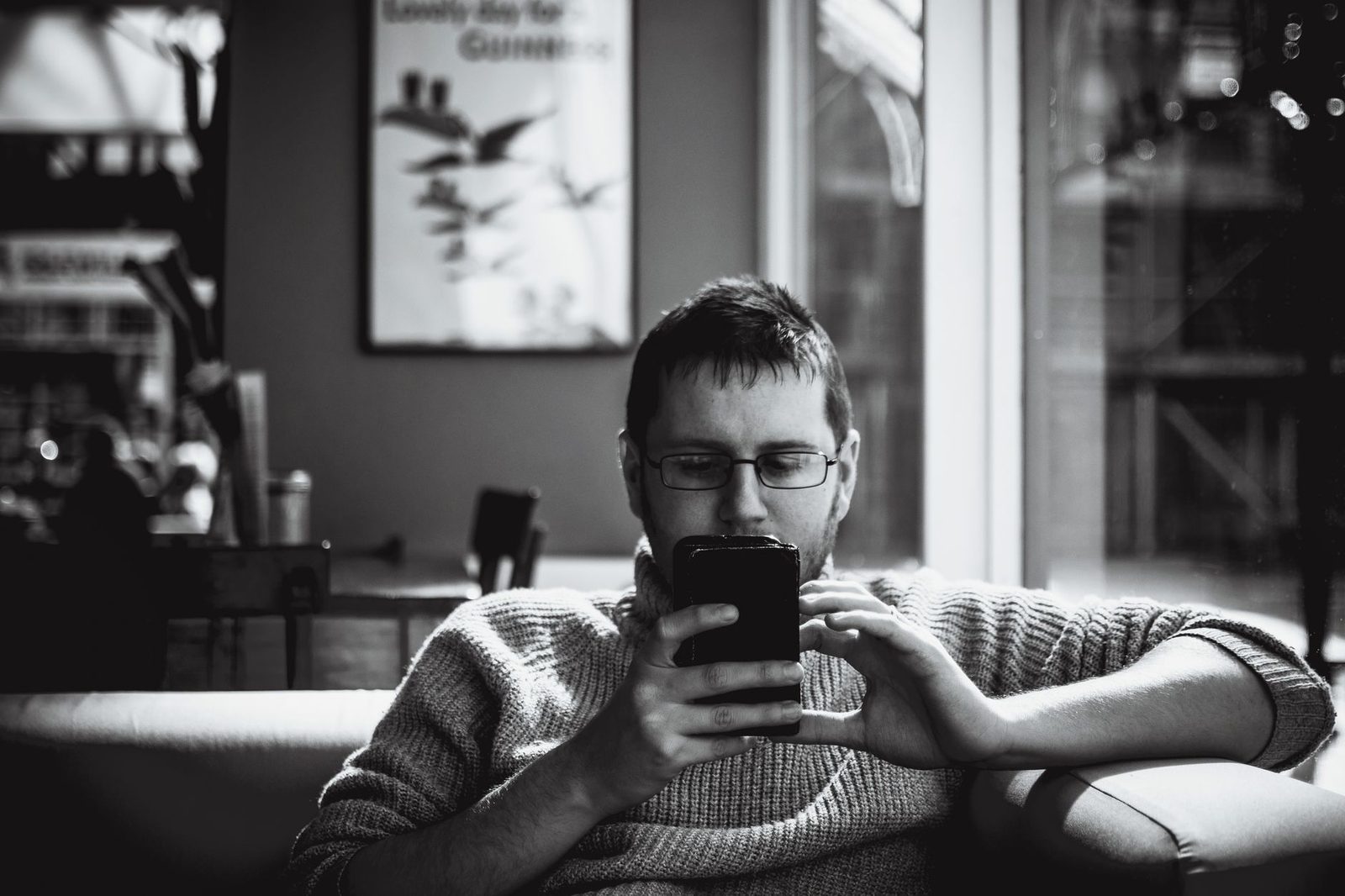 Hombre con gafas sentado en un sofá, mirando su teléfono móvil, fotografía en blanco y negro