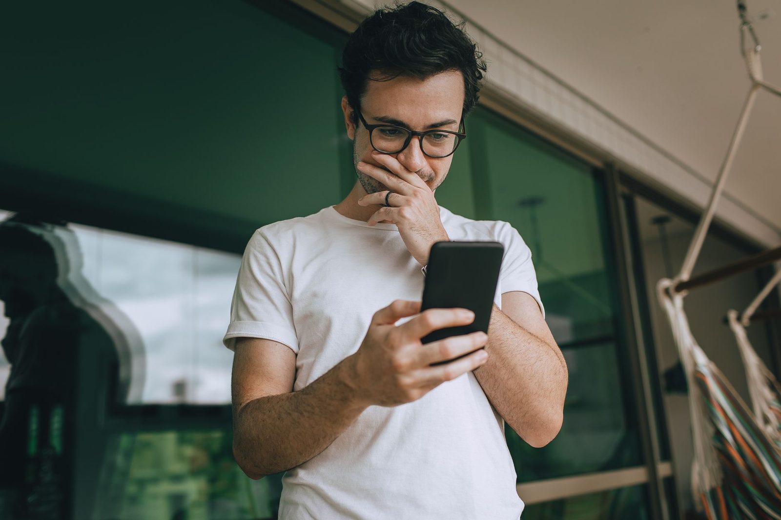 Mann mit Brille, Hand vor dem Mund, der besorgt auf sein Smartphone blickt