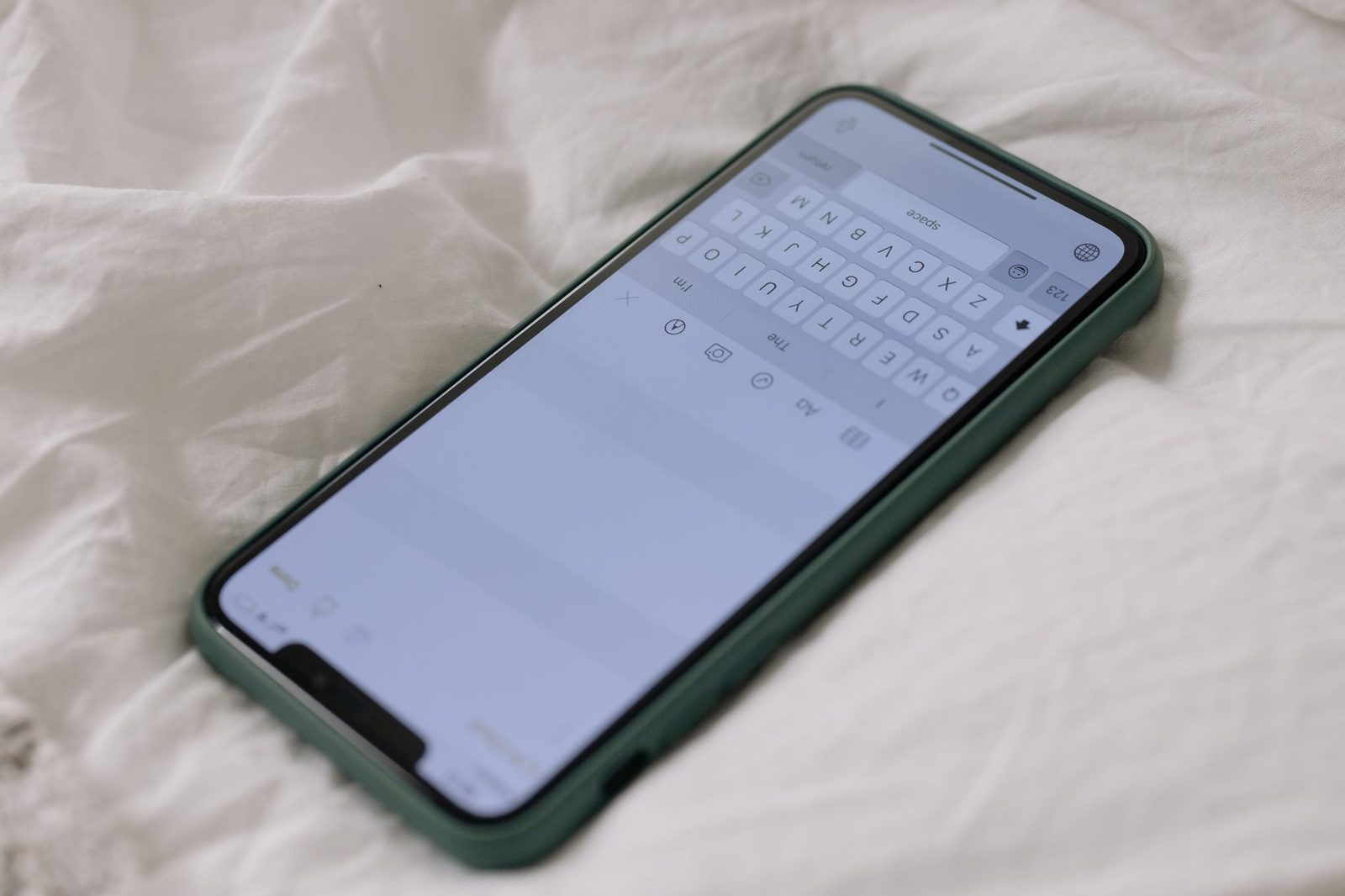 Smartphone avec coque verte posé sur un drap blanc, clavier de messagerie affiché à l'écran