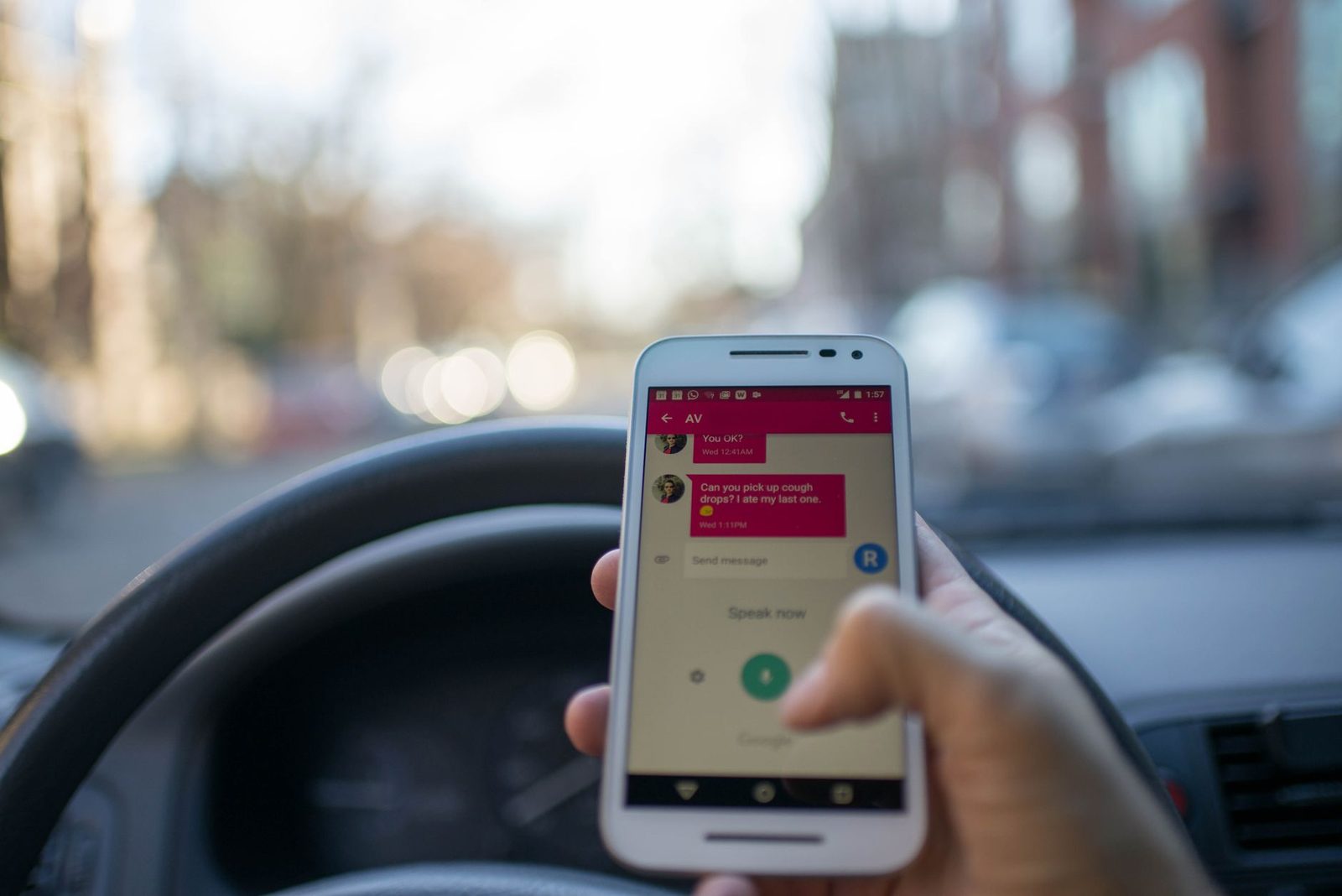 Main tenant un smartphone affichant une conversation SMS, au volant d'une voiture en ville