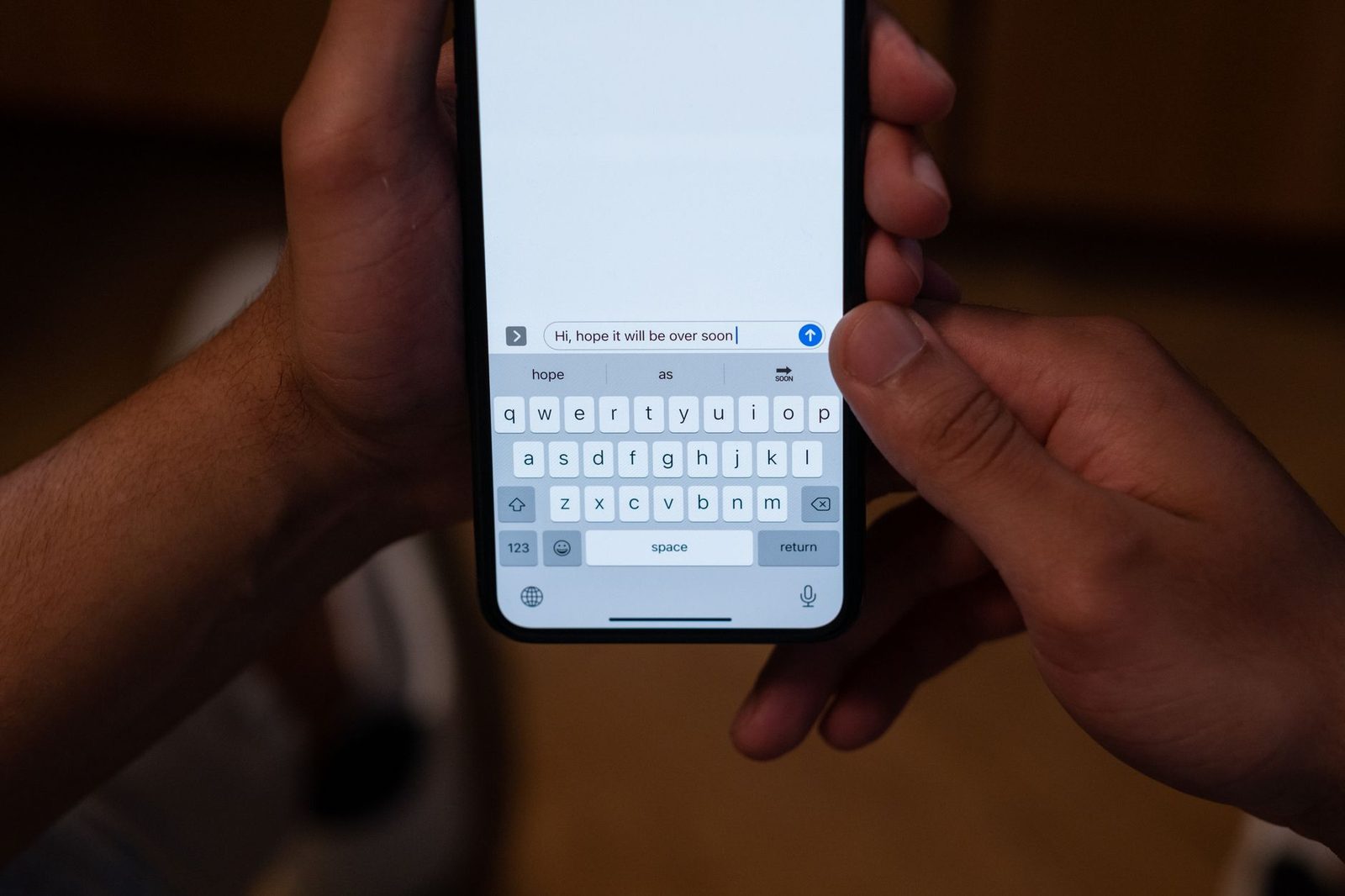 Mains tenant un smartphone affichant un clavier et un message texte en cours de rédaction
