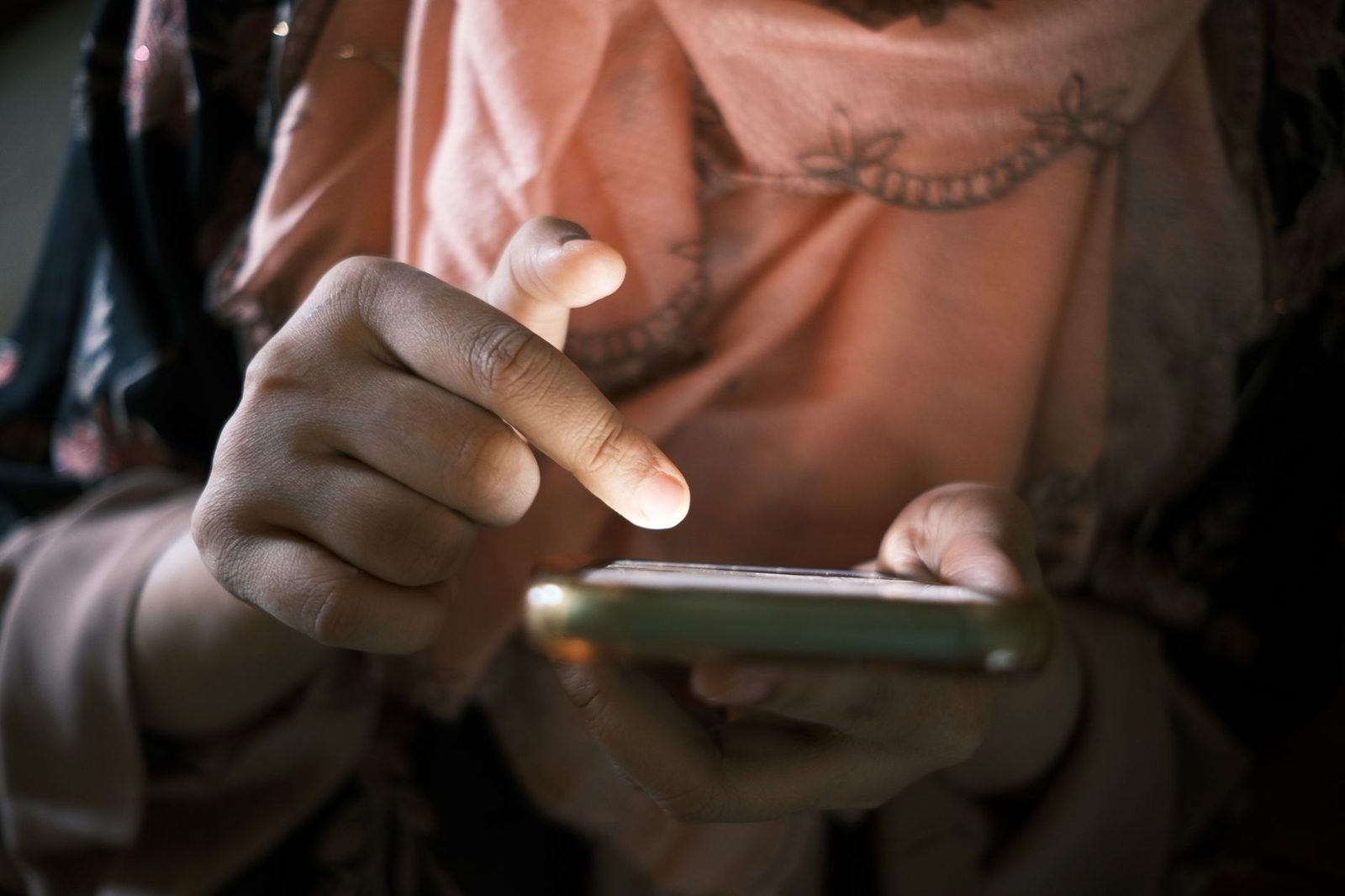 Primo piano delle mani di una donna che tocca lo schermo dello smartphone in una stanza buia