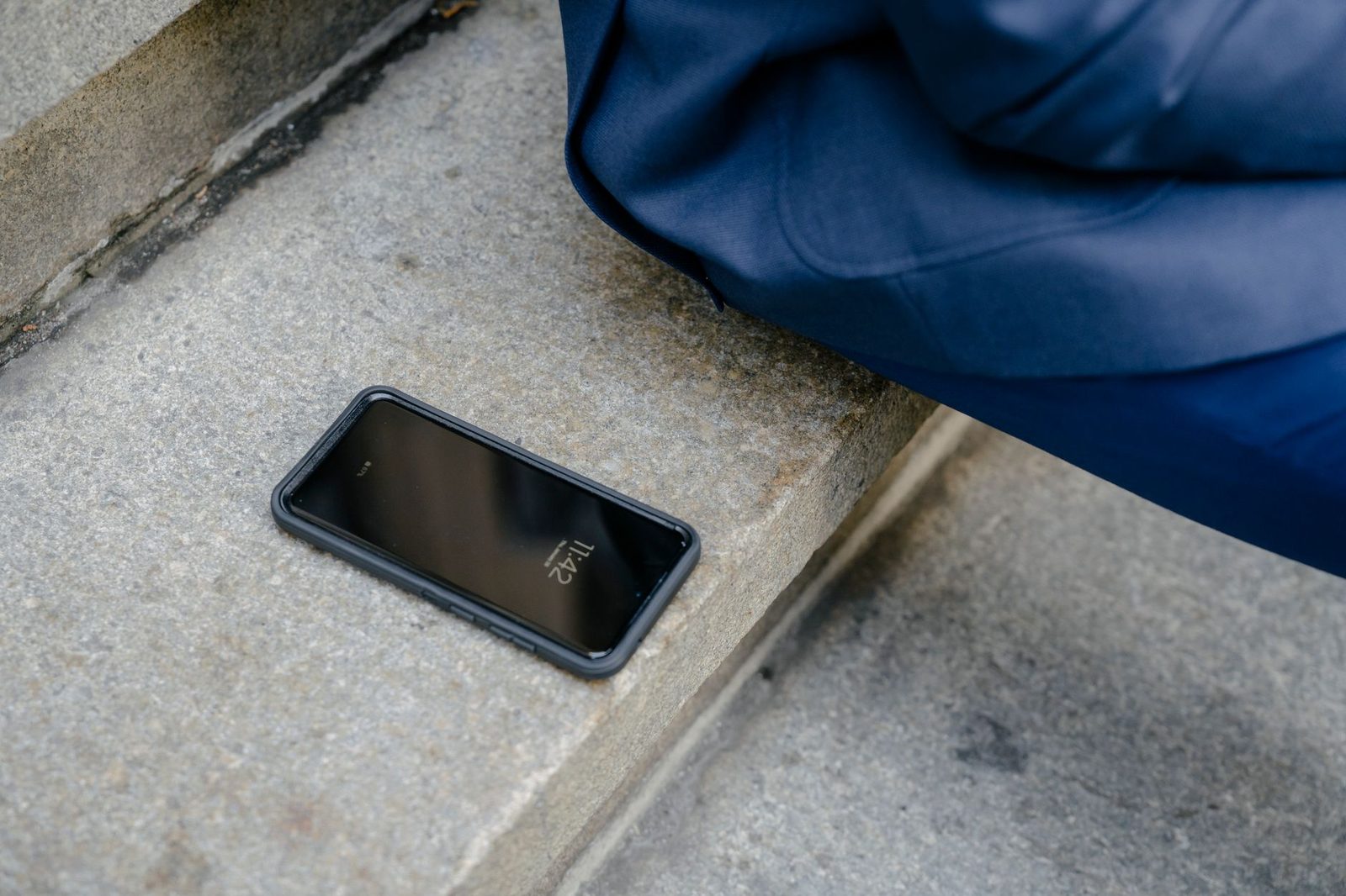 Smartphone nero con schermo spento appoggiato su un gradino di pietra, vicino a un tessuto blu
