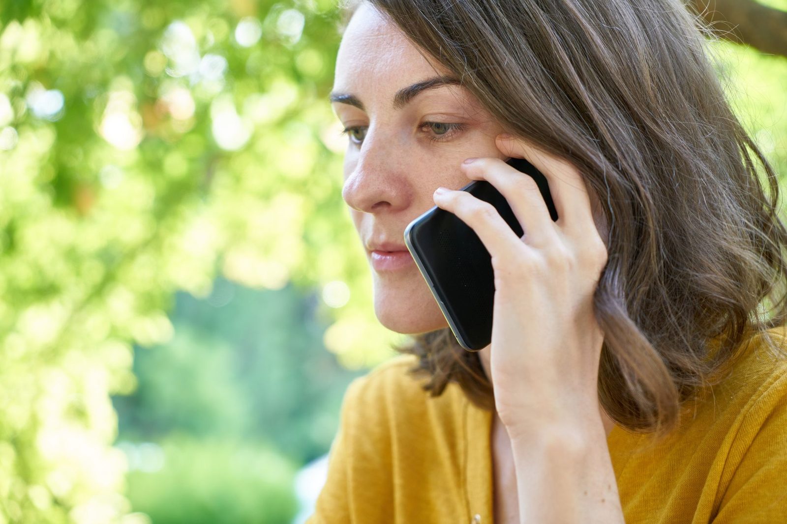 Donna con gilet giallo al telefono, smartphone all'orecchio, espressione preoccupata, all'aperto