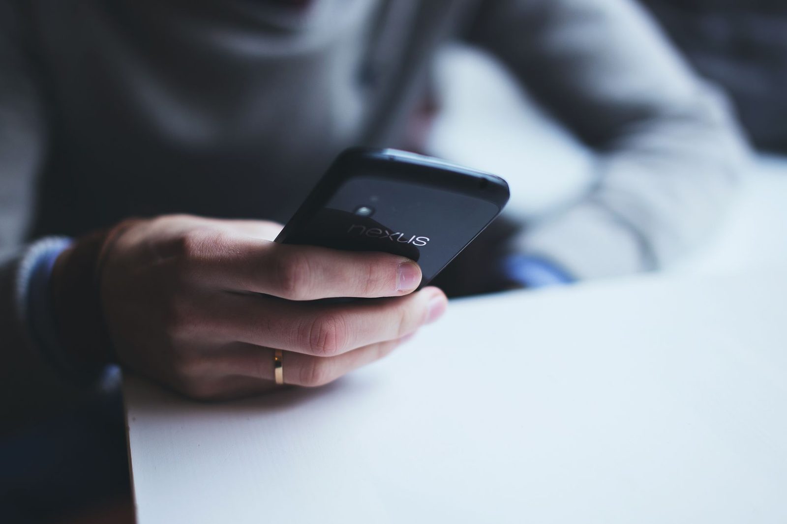 Primo piano della mano di una persona che tiene uno smartphone nero sopra un tavolo bianco