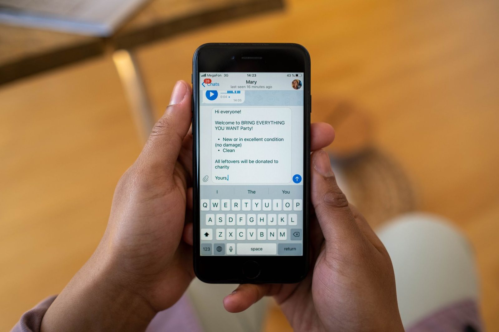 Manos sosteniendo un smartphone que muestra una conversación de mensajería con el teclado abierto