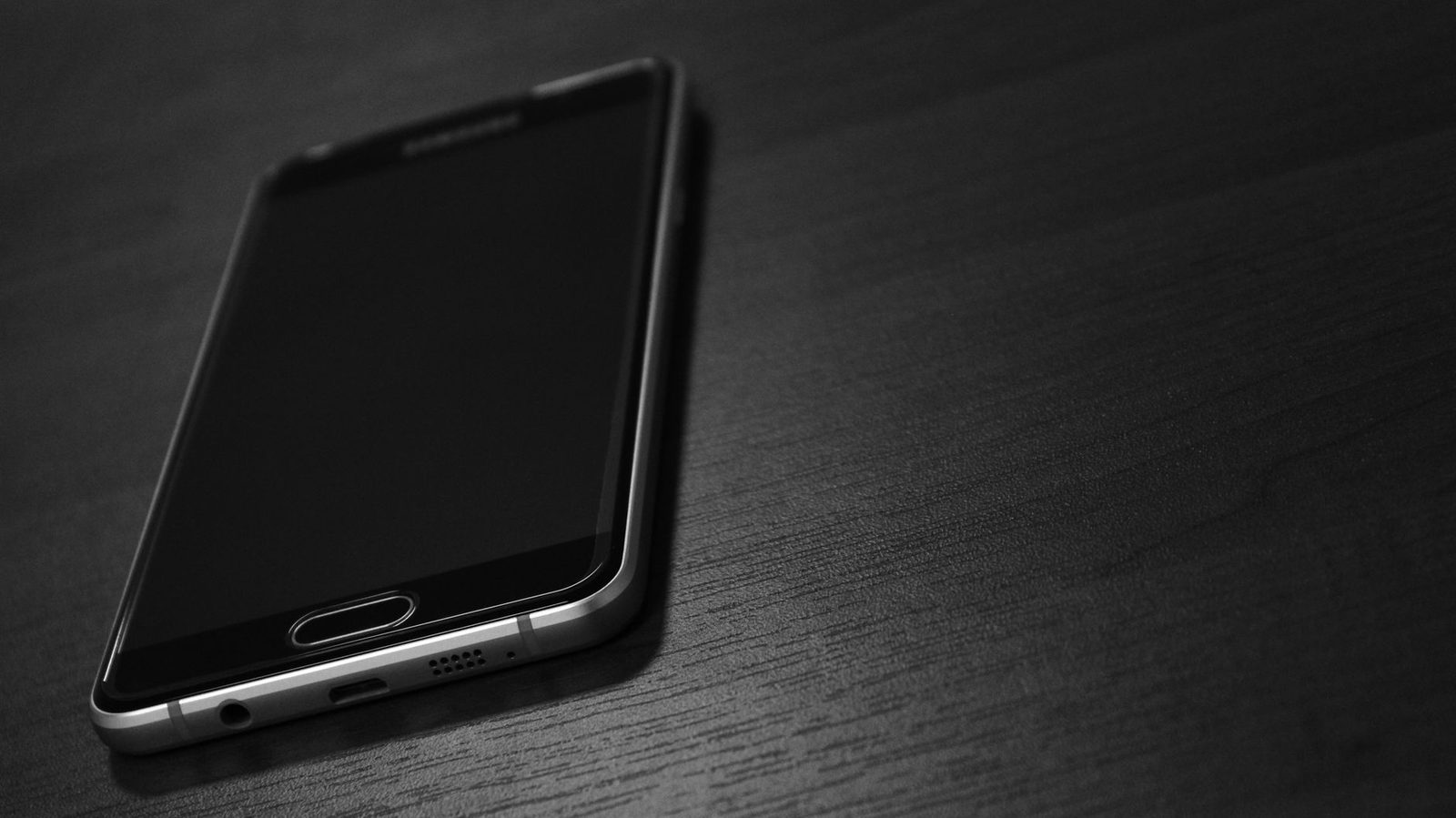 Smartphone à écran éteint posé sur une table en bois sombre, photo en noir et blanc