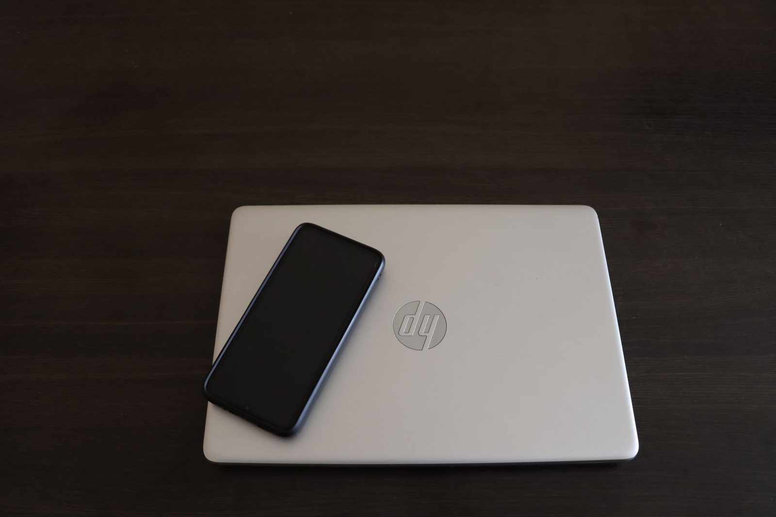 Smartphone noir posé sur un ordinateur portable HP argenté fermé, sur une table en bois sombre