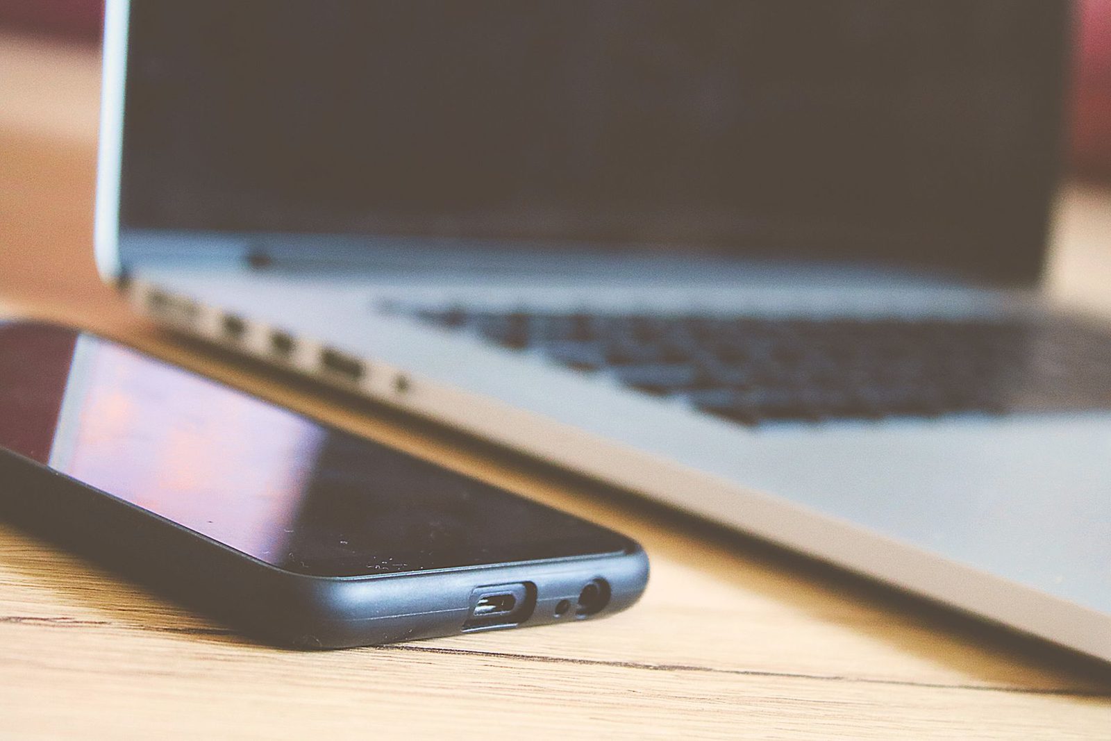 Black smartphone resting on a wooden table next to an open laptop