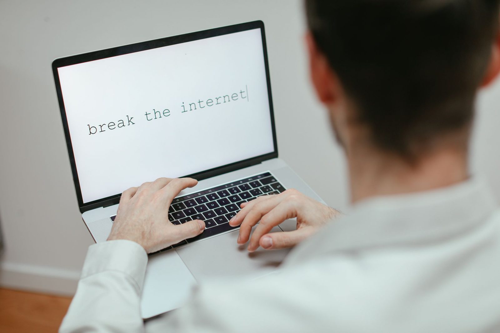 Man seen from behind typing on a laptop keyboard displaying text on the screen
