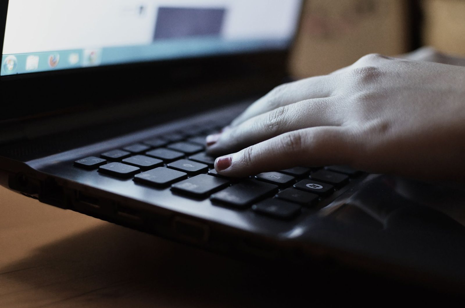 Hand resting on the keyboard of a lit laptop, typing text