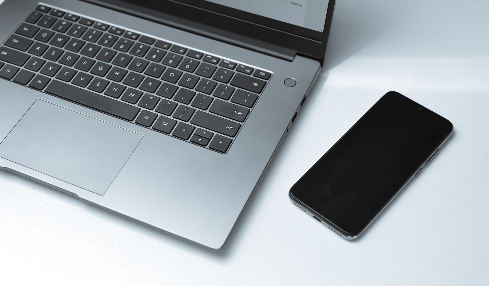 Open laptop and a smartphone with a blank screen side by side on a white desk
